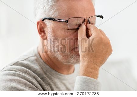 stress, old age and people concept - close up of senior man in glasses having headache and massaging nose bridge