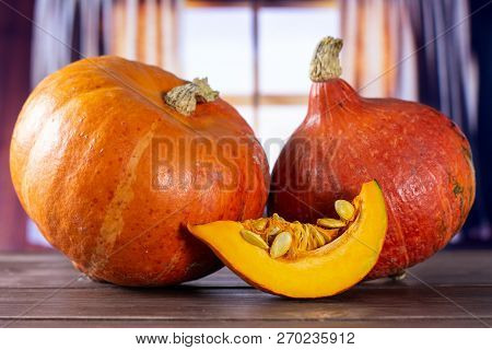Group Of Two Whole One Slice Of Fresh Red Kuri Pumpkin Hokkaido Variety With Silk Curtains Behind