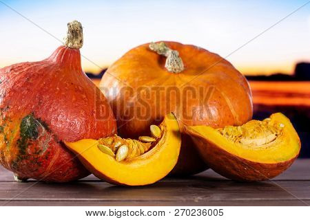 Group Of Two Whole Two Slices Of Fresh Red Kuri Pumpkin Hokkaido Variety With Autumn Field And Sunse