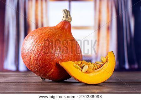 Group Of One Whole One Slice Of Fresh Red Kuri Pumpkin Hokkaido Variety With Silk Curtains Behind