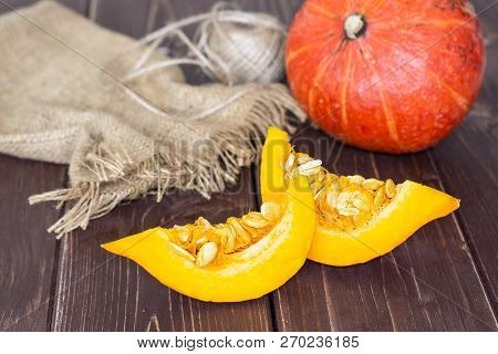 Group Of One Whole Two Slices Of Fresh Red Kuri Pumpkin Hokkaido Variety On Jute Cloth On Brown Wood