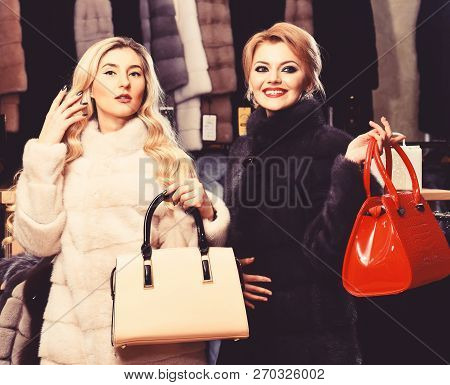 Girls With Smiling Faces In Black And White Fur Coats Hold Purses In Hands. Luxury Style Concept. Wo