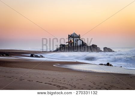 Side View Of Senhor Da Pedra Chapel At Sunset With Waves Crashing In The Sand. Golden Hour. Copy Spa