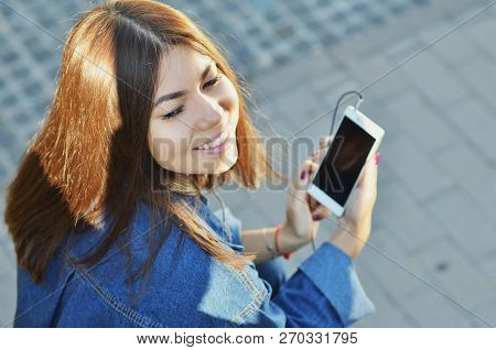 The Girl Sits On A Bench And Listens To Music With Headphones Smiling With Her Eyes Closed