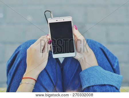 Smartphone Close-up In The Hands Of A Girl Dressed In Denim Clothing That Listens To Music In Headph