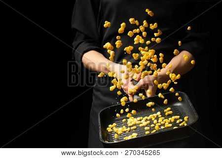 Professional Cook. Chef Is Preparing A Dish With Corn In A Pan. On A Black Background. Menu, Recipe