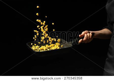 Professional Cook. Chef Is Preparing A Dish With Corn In A Pan. On A Black Background. Menu, Recipe