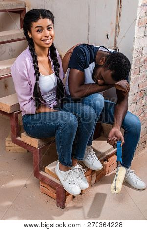 High Angle View Of Attractive Afircan American Woman Cheering Up Exhausted Boyfriend With Paint Roll