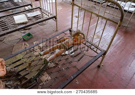 Doll On Metal Grid Of Bed In Abandoned Kindergarten In Destroyed Village Kopachi (10-km Chernobyl Np