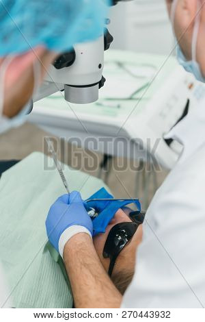 Doctor Used Microscope. Dentist Is Treating Patient In Modern Dental Office. Operation Is Carried Ou