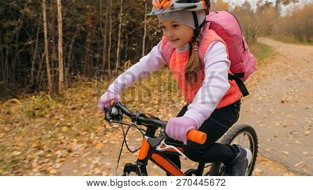 One Caucasian Children Rides Bike Road In Autumn Park. Little Girl Riding Black Orange Cycle In Fore