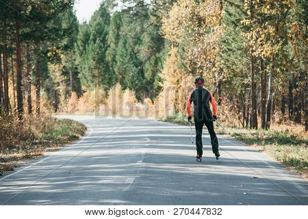 Training An Athlete On The Roller Skaters. Biathlon Ride On The Roller Skis With Ski Poles, In The H