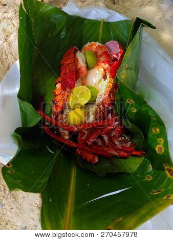A Closeup Of A Freshly Cooked  Red Lobster Is Placed Over A Banana Leaf. There Are Slices Of Lime On