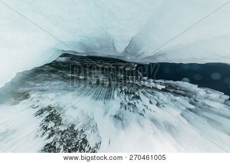 Winter Baikal. Olkhon Island. Ice Grotto. Thick Blue Ice And Icicles On The Coastal Rocks Of Olkhon 