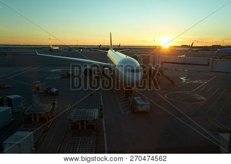 Top Down View Of A Docked Plane At Airport On Sunset With The Golden Light Of The Sun Warming The Sc