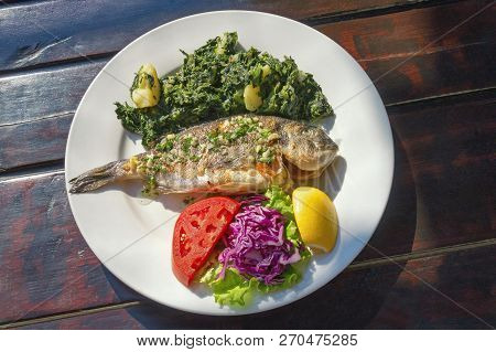 Balkan Cuisine. Grilled Fish ( Sea Bream ) With Vegetables And Slice Of Lemon On White Plate. Dark R