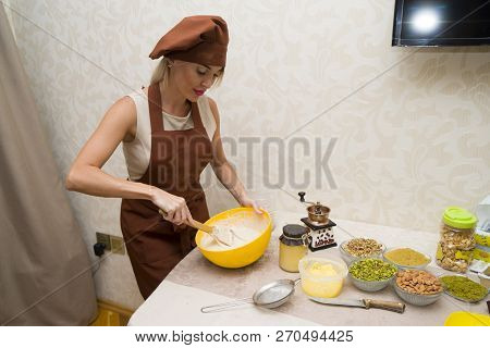 Young Beautiful Woman In An Apron Making Cake With Cream And Berries At The Kitchen