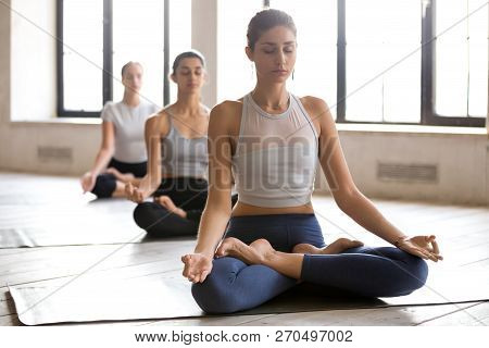 Group Of Young Women Practicing Yoga, Ardha Padmasana Pose