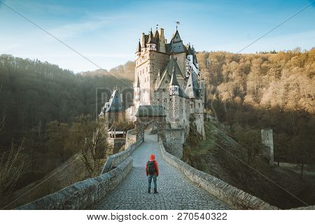 Panorama View Of Young Explorer With Backpack Taking In The View At Famous Eltz Castle At Sunrise In