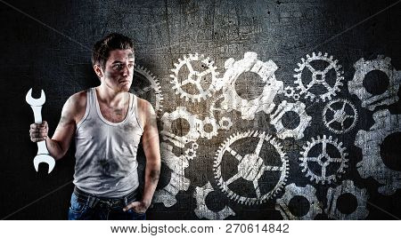 Confused Mechanic Holding A Wrench In Front Of A Blackboard, Drawn With A Engine Wheels Gear.