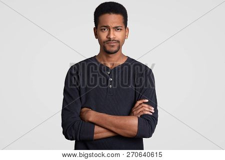 Stusio Shot Of Displeased Man With Unhappy Facial Expression, Keeps Hands Crossed, Feels Upset As He