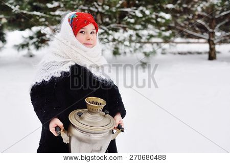 Child Girl In A Fur Coat And Headscarf In Russian Style Holding A Large Samovar On The Background Of