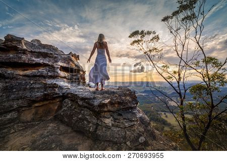 Standing On A Rocky Ledge With Valley Views And Distant Mountains, Dress Blowing In The Wind She Dre