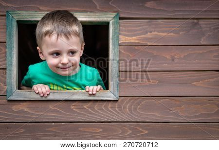 Portrait Of A Cute Little Caucasian Boy Looking Through The Window Of A Wooden Toy House In A Outdoo