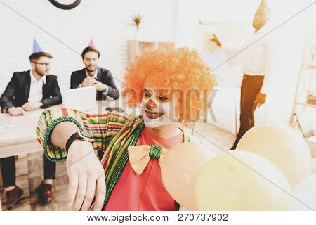 Young Man In Clown Costume On Meeting In Office. Loking At Hand Watch. Clown With Baloons. April Foo