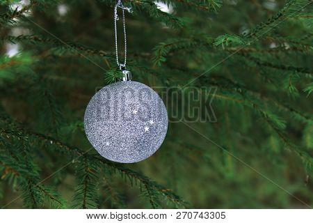 The beautiful decoration on the Christmas tree. Silver shiny Christmas ball on the fir branch. Christmas tree. The spirit of Christmas. Christmas traditions. Winter mood and love