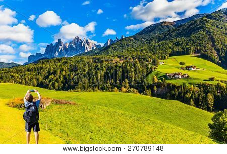 Charming boy with a large backpack photographs South Tyrol with a mobile phone. Delightful mountain valley in the Dolomites. The concept of ecological and photo tourism