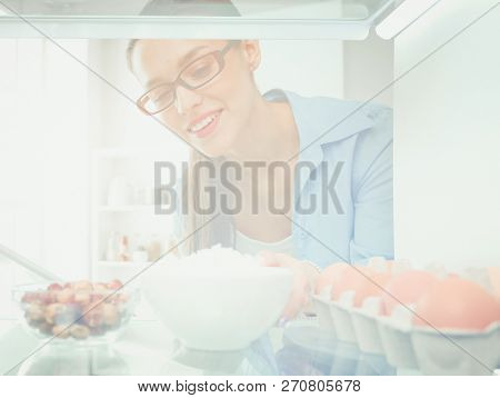 Portrait of female standing near open fridge full of healthy food, vegetables and fruits. Portrait of female