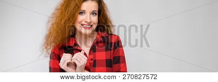 Charming Young Girl Folded Her Arms In The Heart. Young Red-haired Girl In A Red Checkered Shirt
