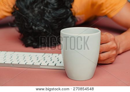 Man Has Burn Out At Work. Head, Keyboard, Smart Phone And Coffee On Pink Table