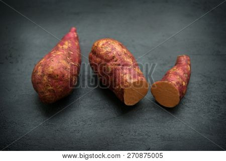 Raw orange sweet potatoes on wooden background close up.