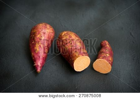 Raw orange sweet potatoes on dark background, close up.