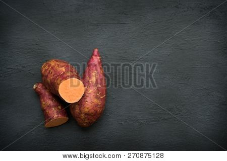 Raw orange sweet potatoes on dark background, Top view close up with copy space.