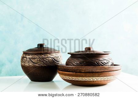 Pots And Plates Of Clay On A White Table And A Blue Background. Clay Pottery Kitchen Utensils Made B