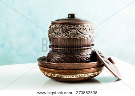 Pots And Plates Of Clay On A White Table And A Blue Background. Clay Pottery Kitchen Utensils Made B