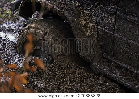 Offroad Tire Covered With Mud Overcomes Obstacles On Nature Background. Wheel In Deep Puddle Of Mud.