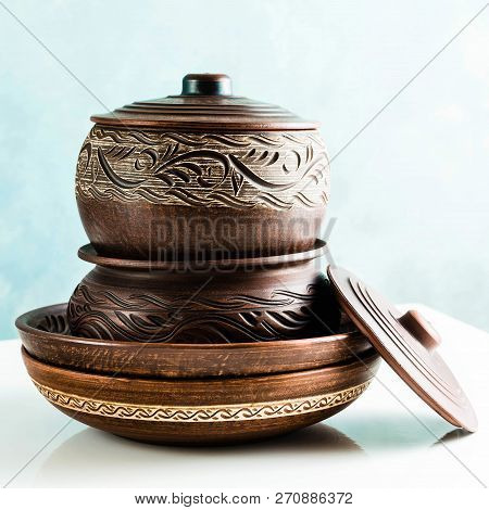 Pots And Plates Of Clay On A White Table And A Blue Background. Clay Pottery Kitchen Utensils Made B