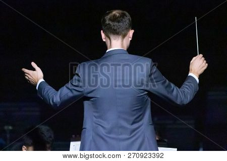 Male Conductor In Grey Suit Working With His Band