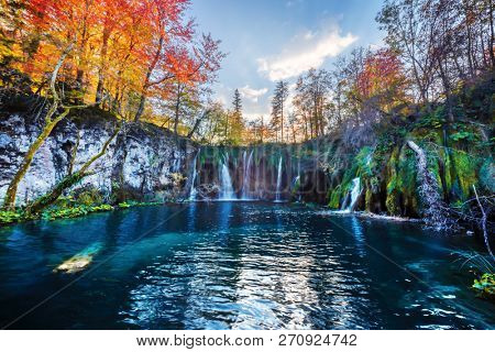 Amazing waterfall with pure blue water in Plitvice lakes. Orange autumn forest on background. Plitvice National Park, Croatia. Landscape photography