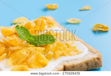 Cornflakes On Yogurt On Bread With Peppermint On Blue Pastel Background Left. Cereal Breakfast Bread