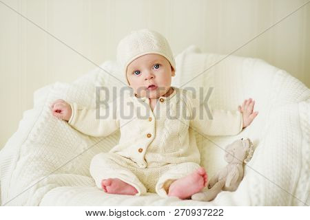 Sweet Baby Wearing Knitted Suit Is Sitting On The Arm-chair