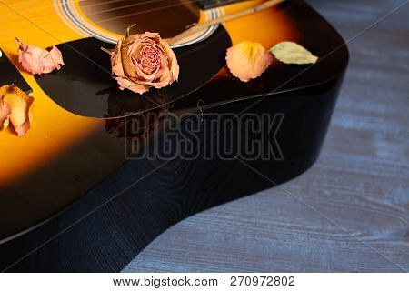 Acoustic Guitar With Dried Roses On The Wooden Table. Template For Advertising A Concert Of Memory O