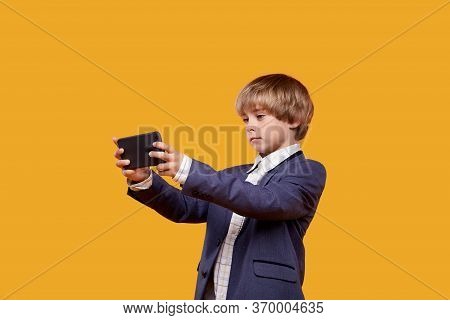 A Little Boy Plays Mobile Games. A Boy In A White Shirt And A Gray Suit.