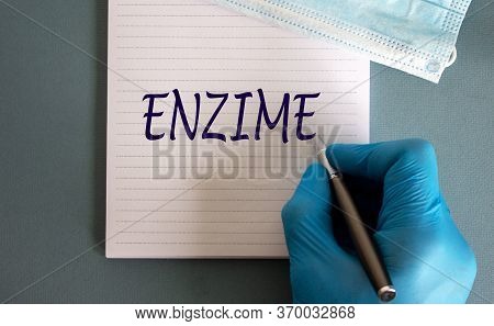 Male Hand In Blue Glove Writes The Word 'enzime' On A White Note. Medicine Mask.