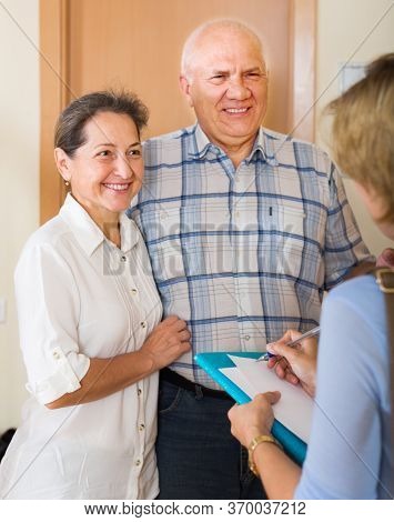 Mature Couple Answering The Questions Of Young Employee In Door At Home