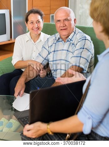 Aged Couple Answer Questions Of Social Worker With Laptop At Home And Smiling. Focus On Man.